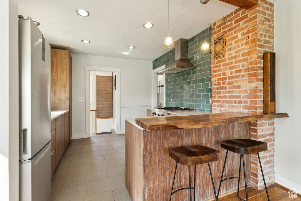 Kitchen with a peninsula, freestanding refrigerator, wall chimney exhaust hood, baseboards, and modern cabinets
