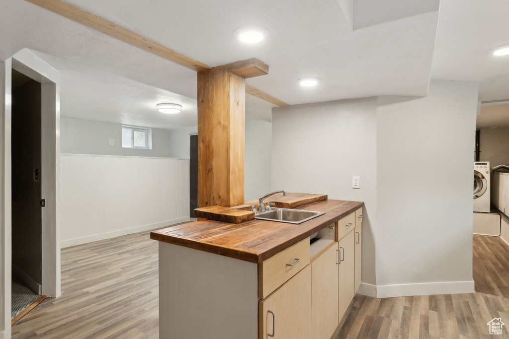 Kitchen featuring washer / clothes dryer, light wood-style flooring, baseboards, a sink, and wood counters
