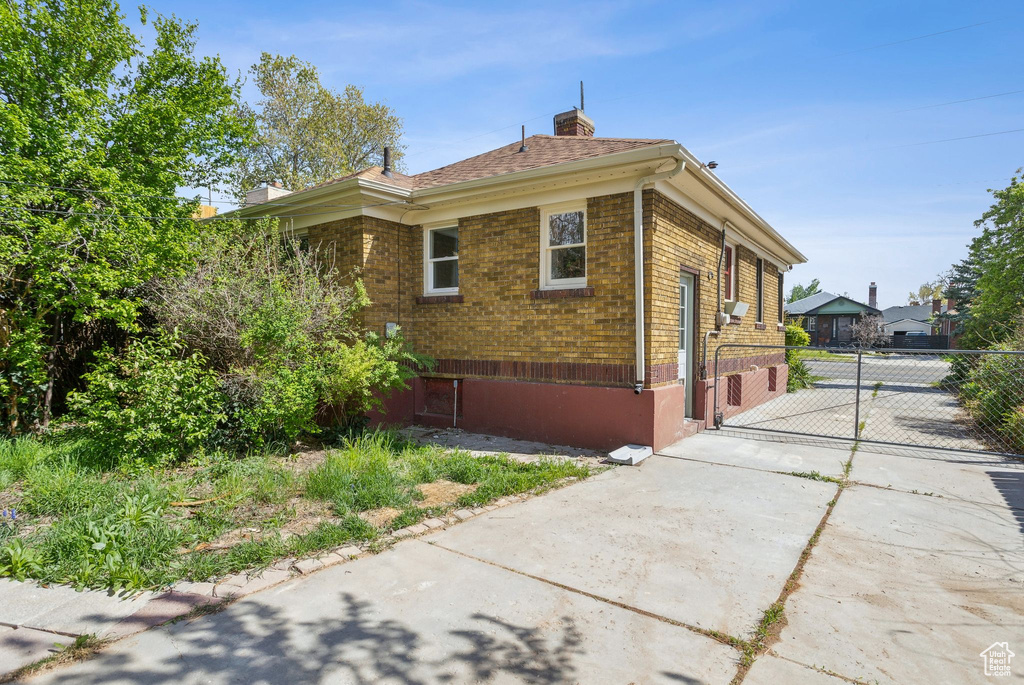 View of side of property with concrete driveway, a chimney, brick siding, and fence