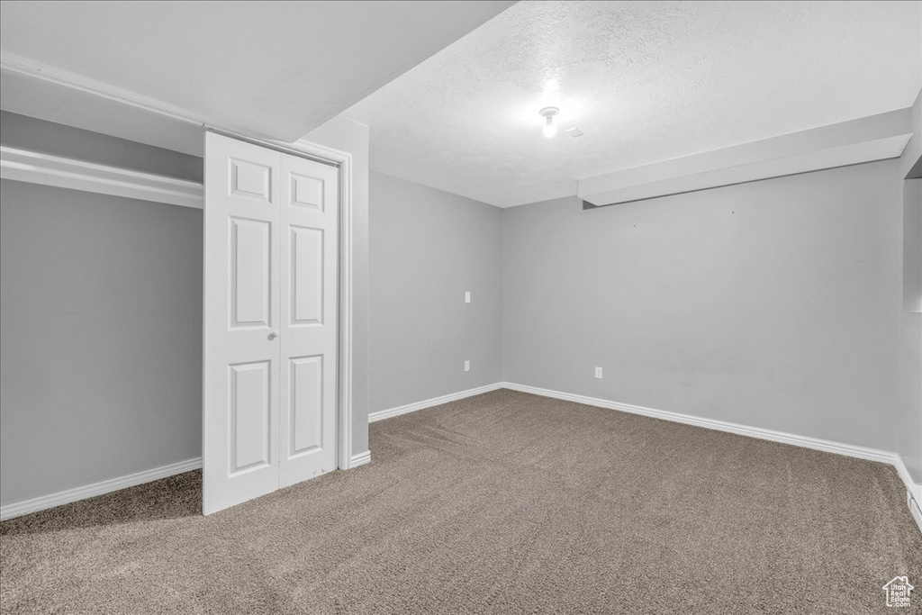 Finished below grade area with carpet flooring, baseboards, and a textured ceiling
