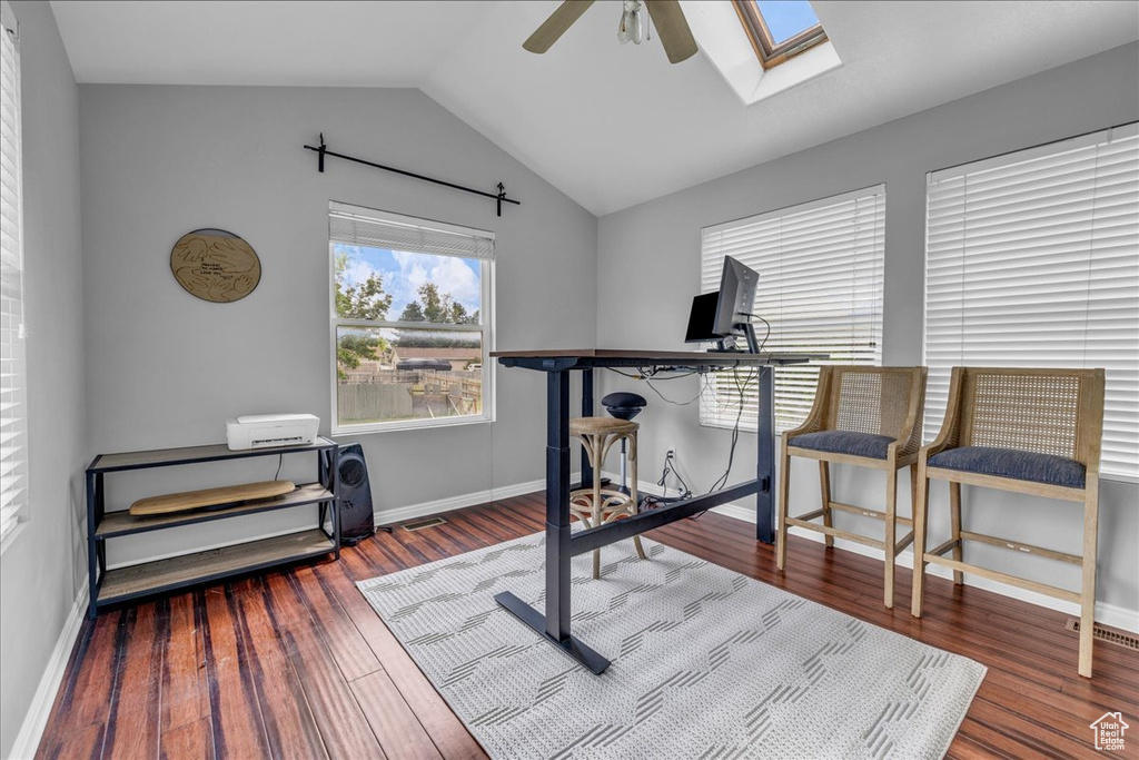 Office featuring ceiling fan, a skylight, vaulted ceiling, wood finished floors, and baseboards