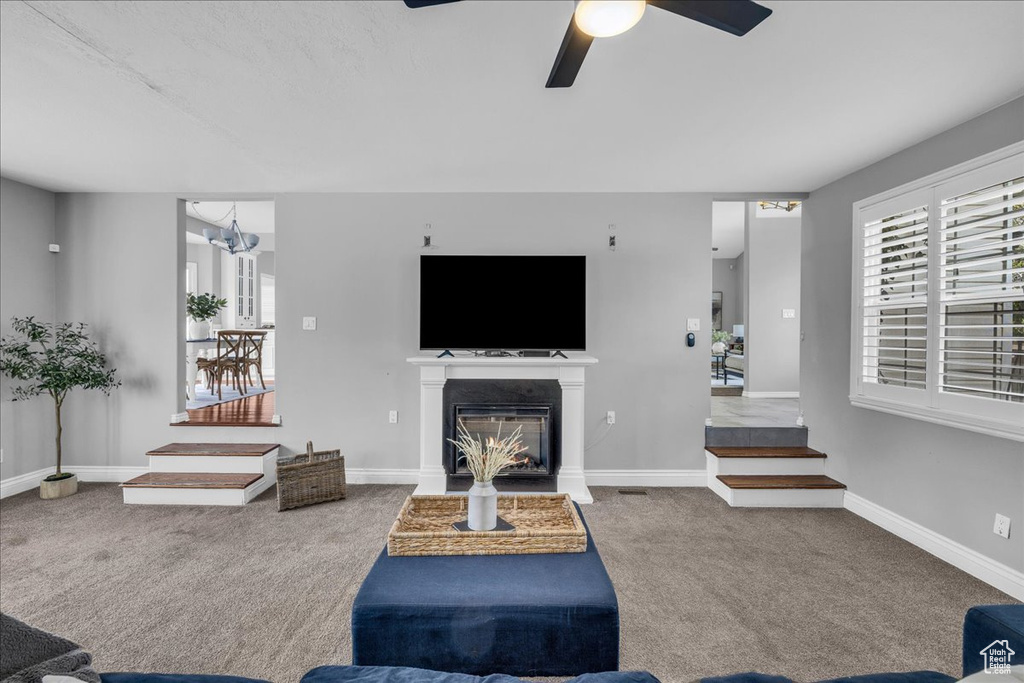 Living room featuring carpet, ceiling fan, a glass covered fireplace, baseboards, and a chandelier