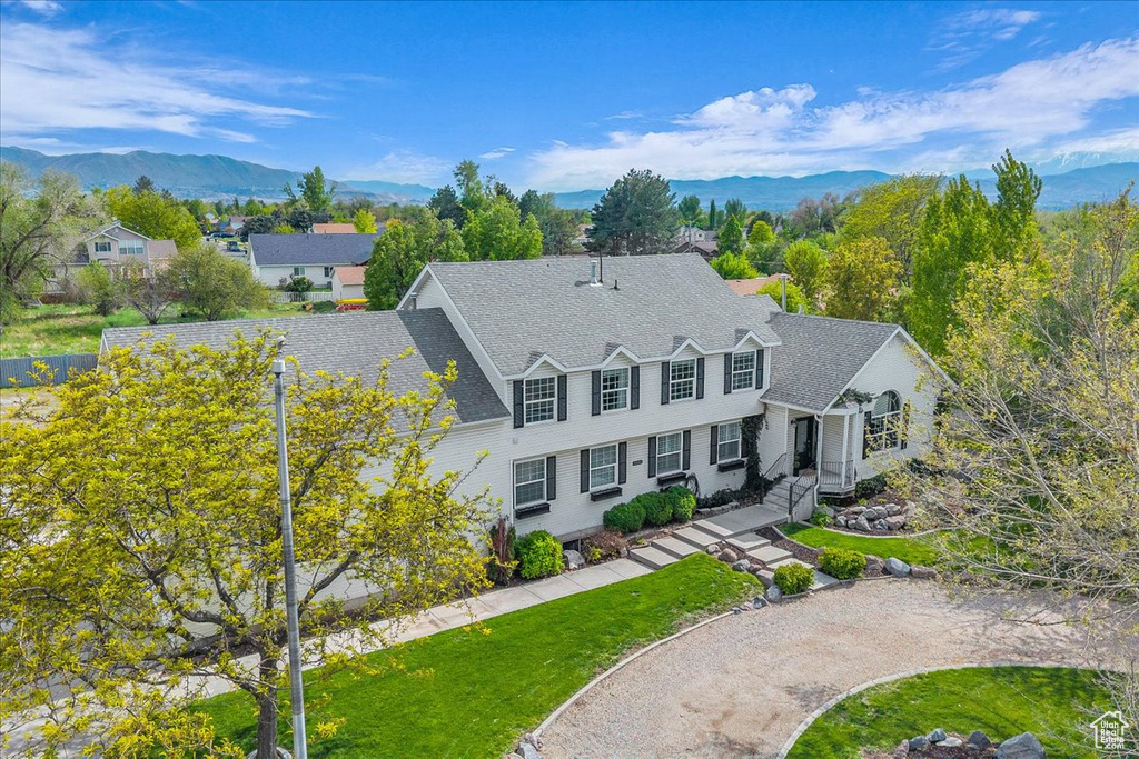 View of front of house with a front lawn, a mountain view, and a shingled roof