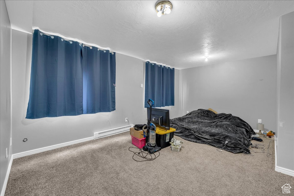 Unfurnished bedroom featuring baseboard heating, carpet flooring, a textured ceiling, and baseboards