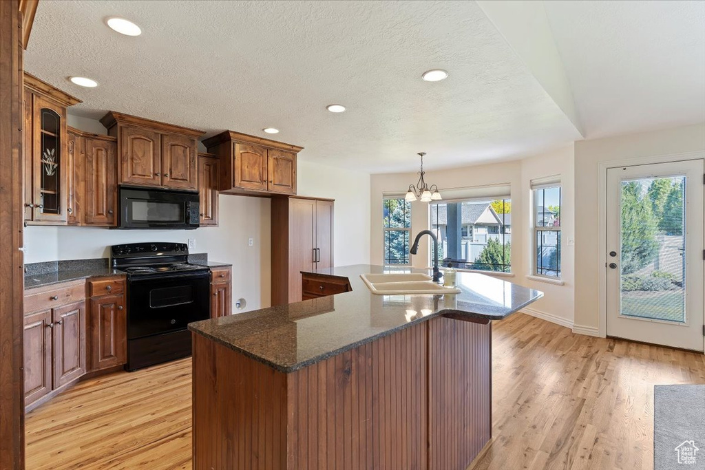 Kitchen with black appliances, light wood-style flooring, a sink, recessed lighting, and a kitchen island with sink
