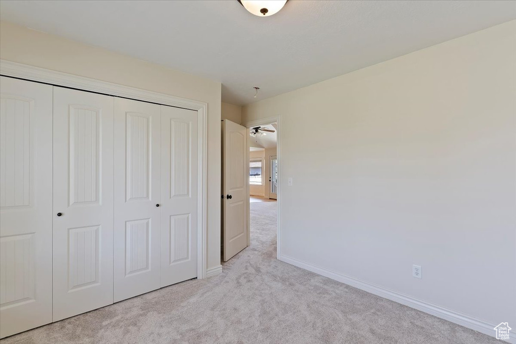 Unfurnished bedroom featuring light carpet, a closet, and baseboards