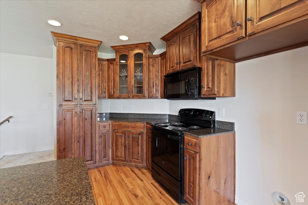 Kitchen with black appliances, glass insert cabinets, dark stone counters, brown cabinetry, and recessed lighting