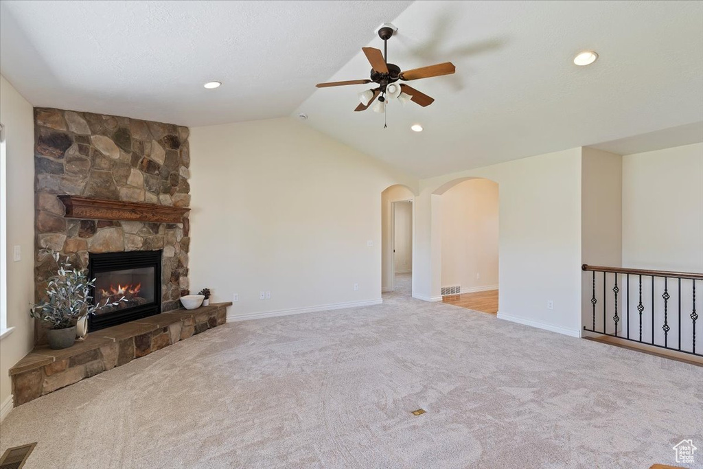 Unfurnished living room featuring ceiling fan, arched walkways, carpet, vaulted ceiling, and a stone fireplace