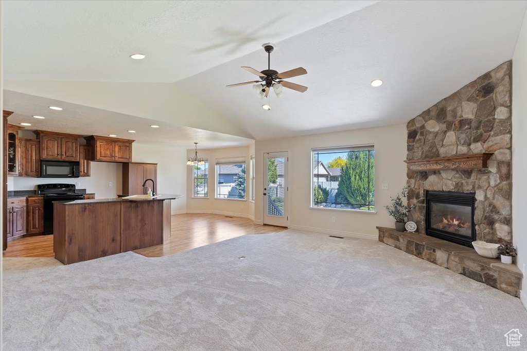Kitchen with black appliances, open floor plan, light carpet, vaulted ceiling, and a fireplace