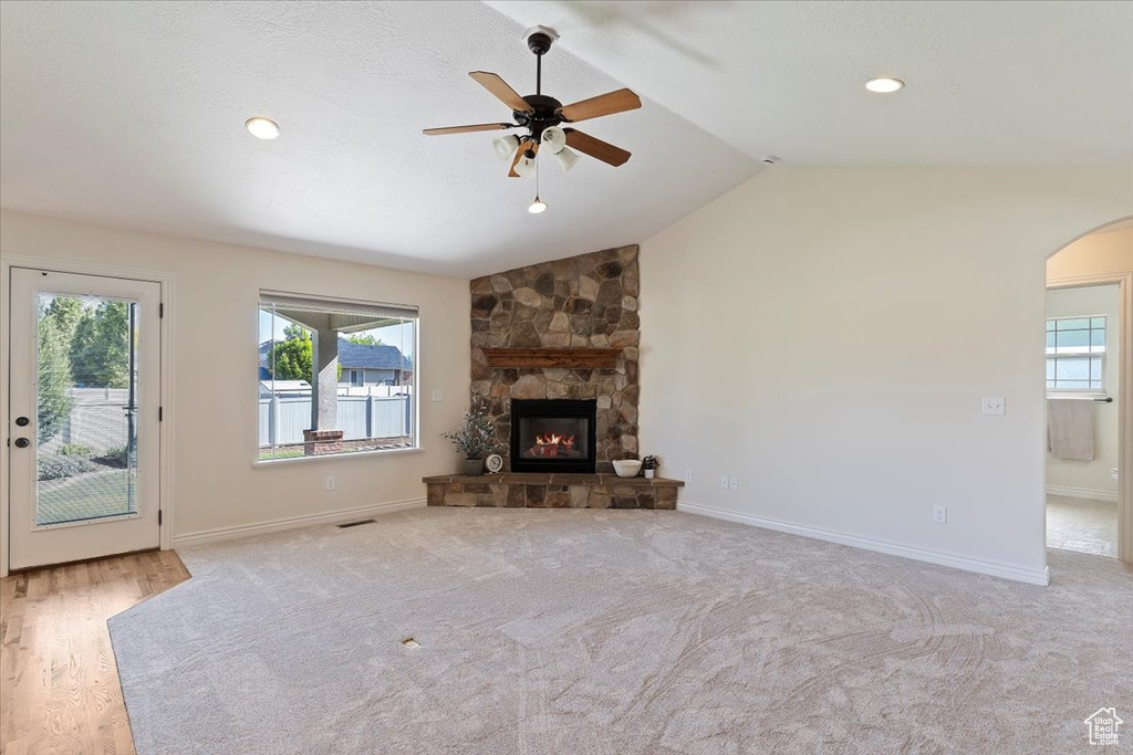 Unfurnished living room featuring arched walkways, a ceiling fan, healthy amount of natural light, a stone fireplace, and vaulted ceiling