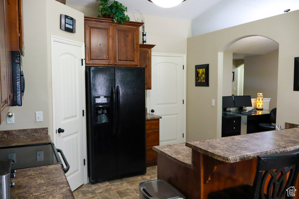 Kitchen with a peninsula, a breakfast bar, black appliances, arched walkways, and dark countertops