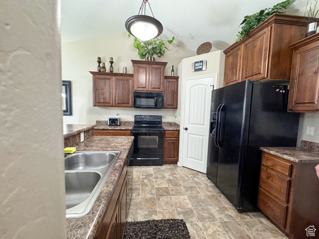 Kitchen with stone finish flooring, a sink, a textured ceiling, black appliances, and lofted ceiling