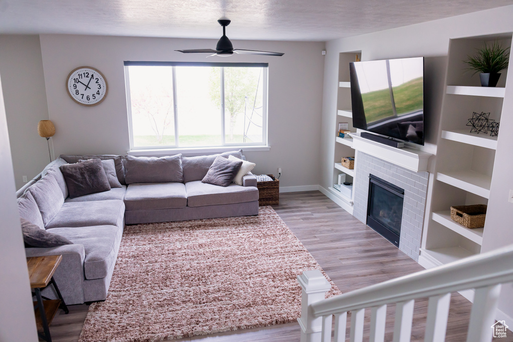 Living area with ceiling fan, light wood-style flooring, a fireplace, baseboards, and built in features