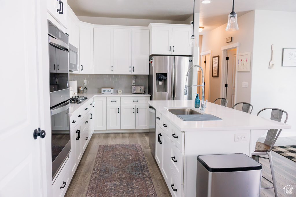 Kitchen featuring appliances with stainless steel finishes, a kitchen breakfast bar, light wood finished floors, a sink, and backsplash