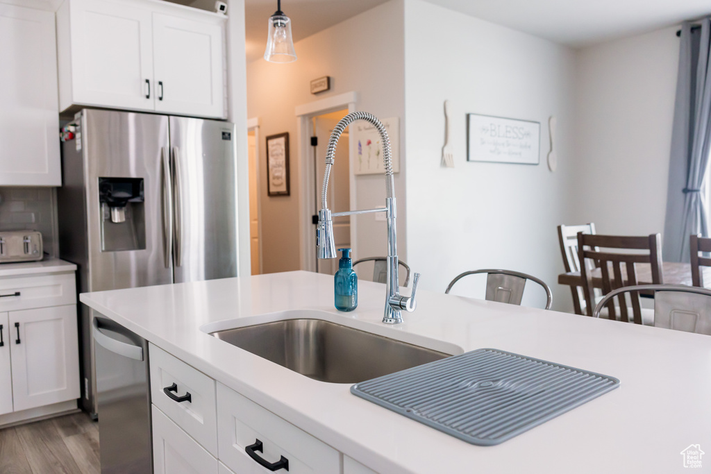 Kitchen featuring stainless steel fridge with ice dispenser, light countertops, a sink, white cabinets, and light wood-style floors