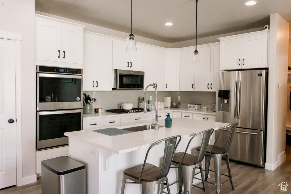 Kitchen featuring appliances with stainless steel finishes, dark wood-type flooring, light countertops, white cabinetry, and recessed lighting