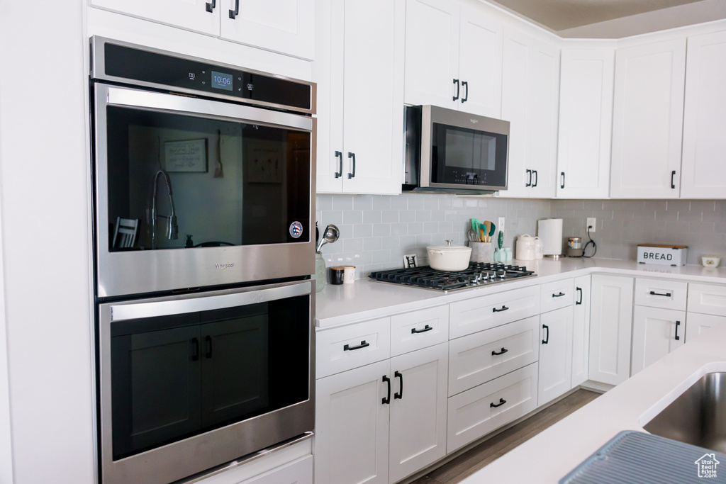 Kitchen with stainless steel appliances, light countertops, white cabinets, and tasteful backsplash