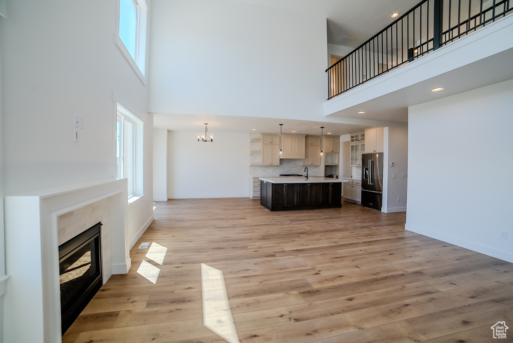 Unfurnished living room featuring a high ceiling, a tiled fireplace, baseboards, light wood finished floors, and a chandelier