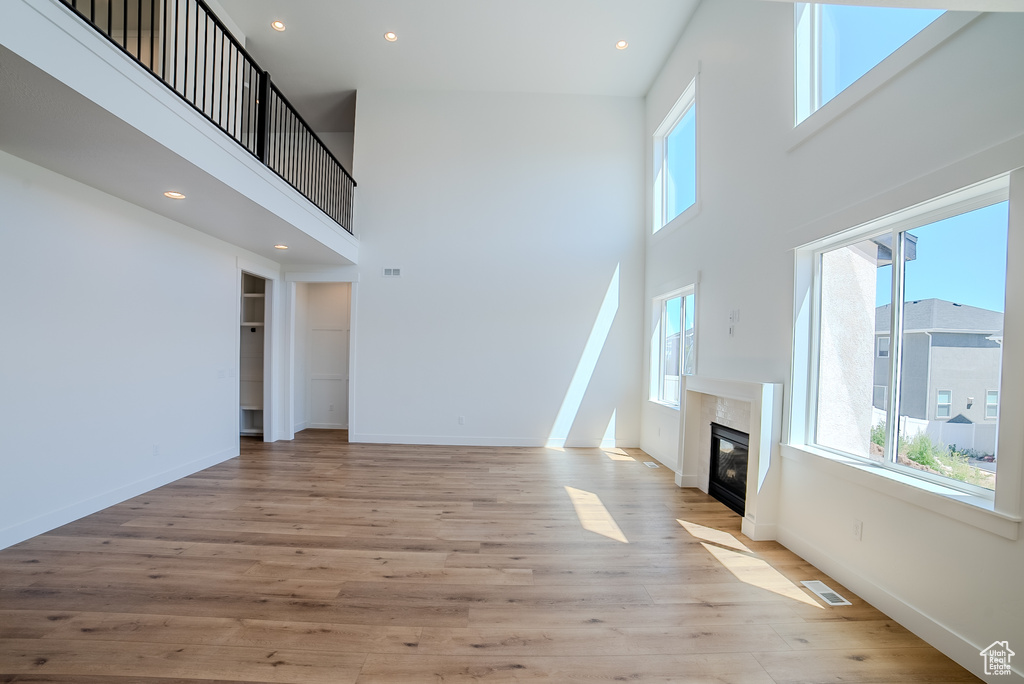 Unfurnished living room with plenty of natural light, a high ceiling, light wood-style floors, a fireplace, and recessed lighting