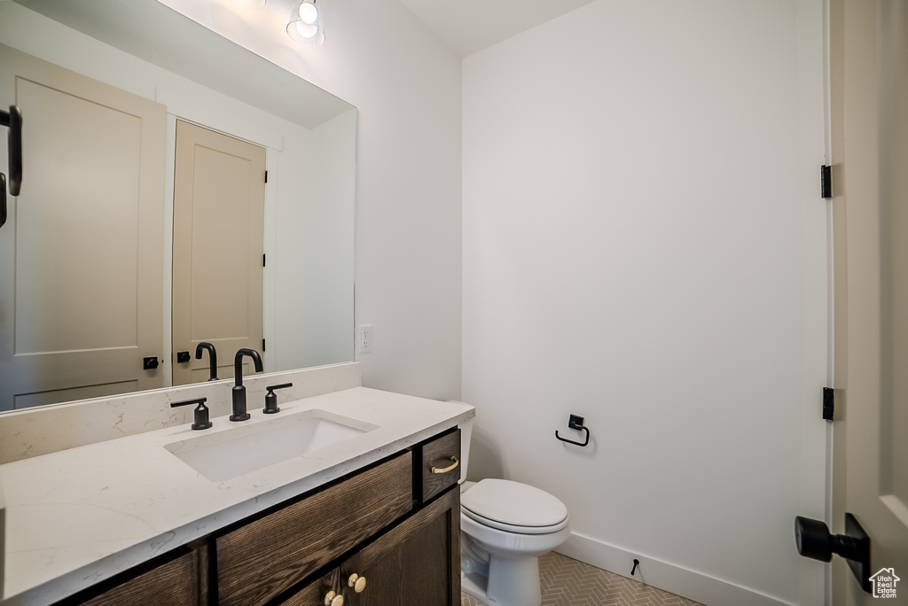 Half bathroom with toilet, vanity, tile patterned floors, and baseboards