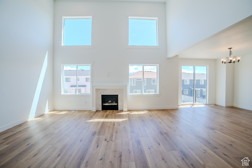 Unfurnished living room with a chandelier, hardwood / wood-style flooring, a high ceiling, a fireplace with flush hearth, and baseboards