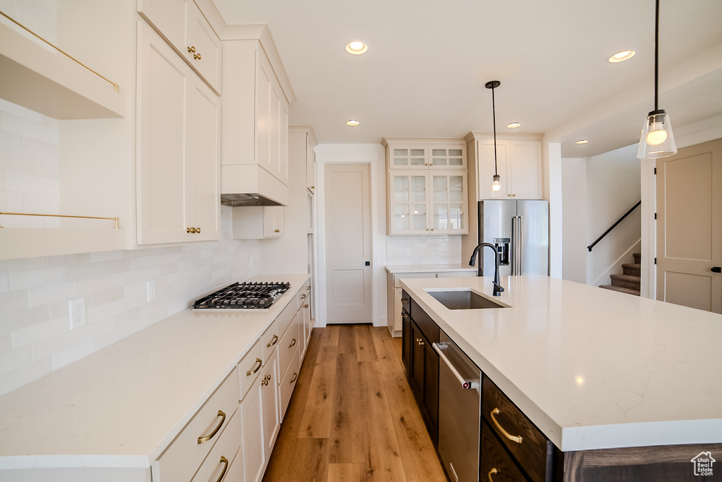 Kitchen with stainless steel appliances, a sink, an island with sink, light wood-style floors, and recessed lighting