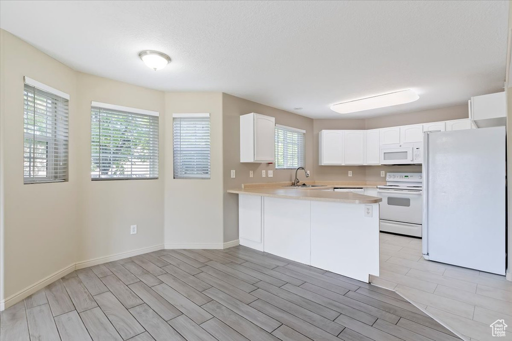 Kitchen with a peninsula, white appliances, light countertops, white cabinets, and a sink