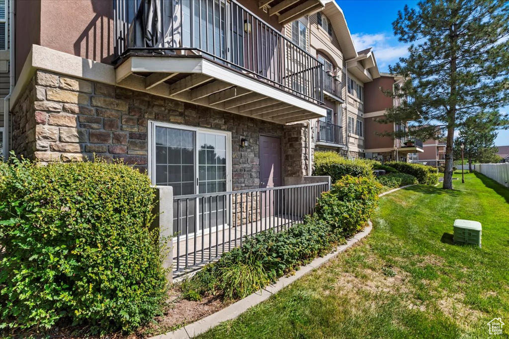View of side of property featuring fence, a balcony, stone siding, stucco siding, and a lawn