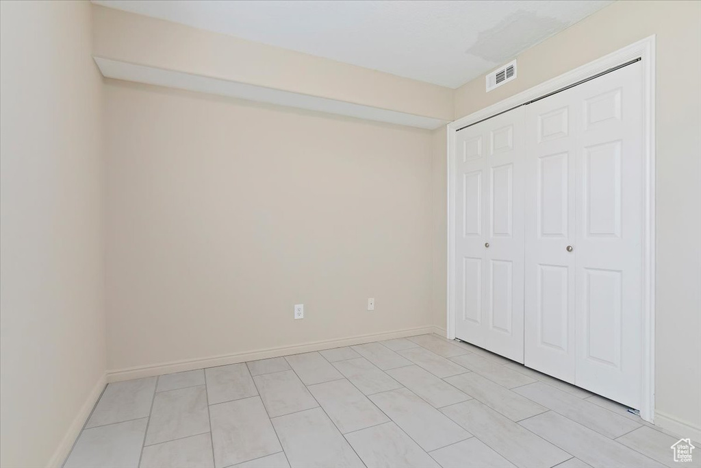 Unfurnished bedroom with baseboards, visible vents, light tile patterned floors, and a closet
