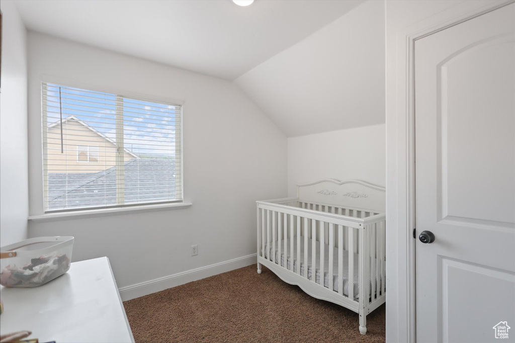 Bedroom featuring carpet, lofted ceiling, a nursery area, and baseboards