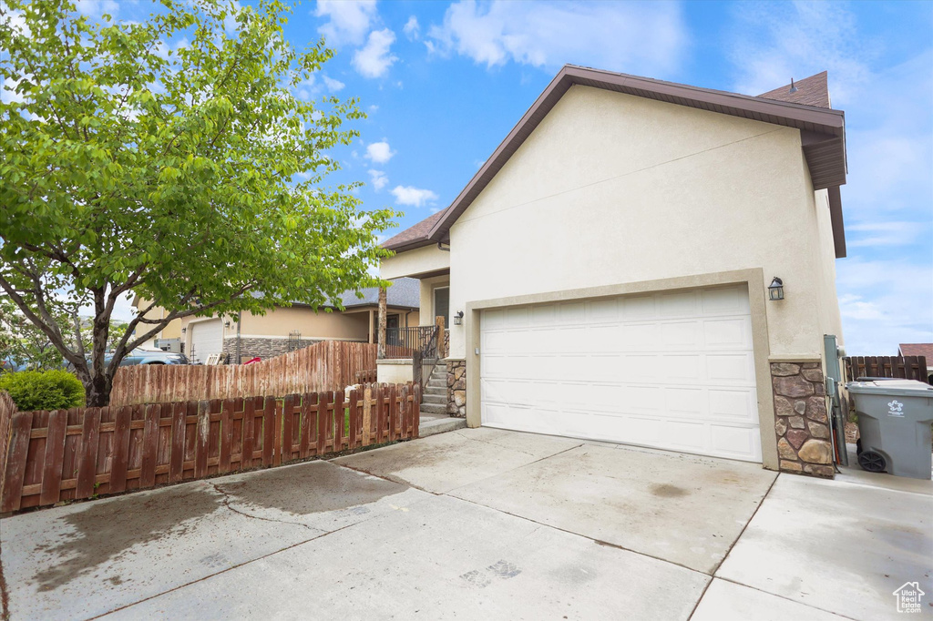 View of property exterior featuring stone siding, stucco siding, driveway, and fence