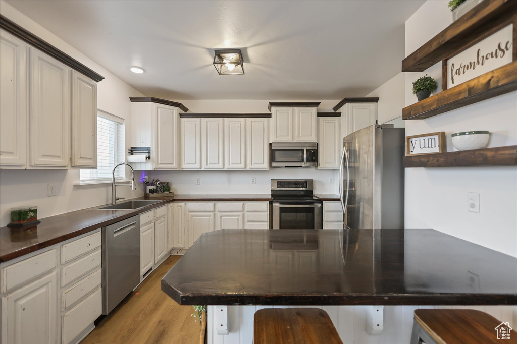 Kitchen with stainless steel appliances, a sink, open shelves, dark countertops, and a kitchen breakfast bar
