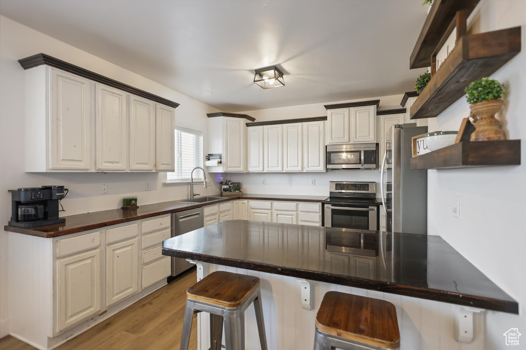 Kitchen featuring appliances with stainless steel finishes, a sink, a breakfast bar area, light wood finished floors, and a peninsula