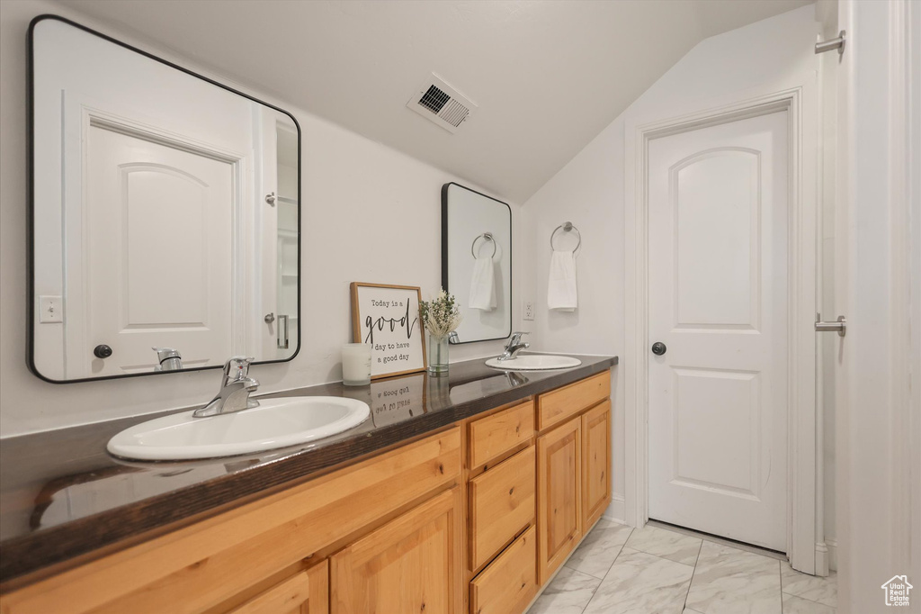 Full bath featuring lofted ceiling, marble look tiles, and double vanity