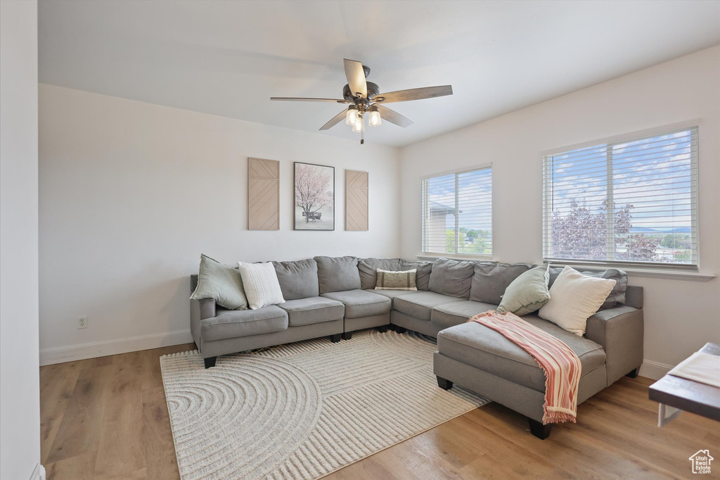 Living room with a ceiling fan, light wood-style flooring, and baseboards
