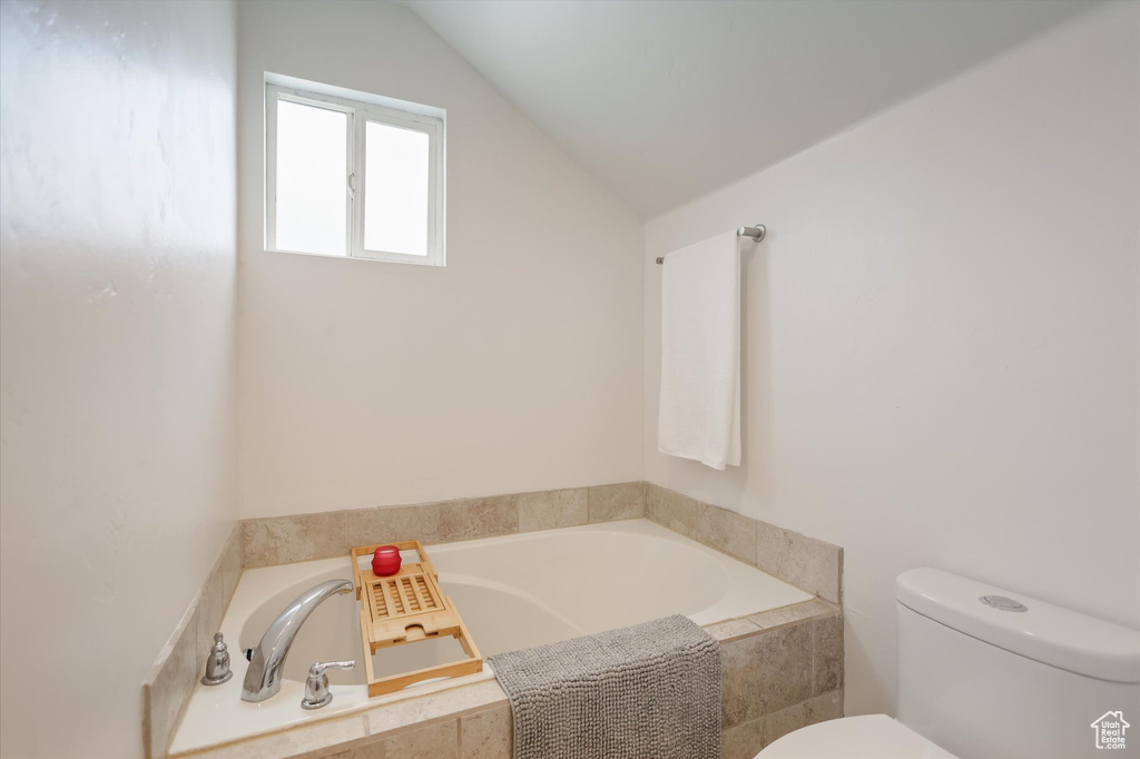Full bath featuring toilet, vaulted ceiling, and a garden tub