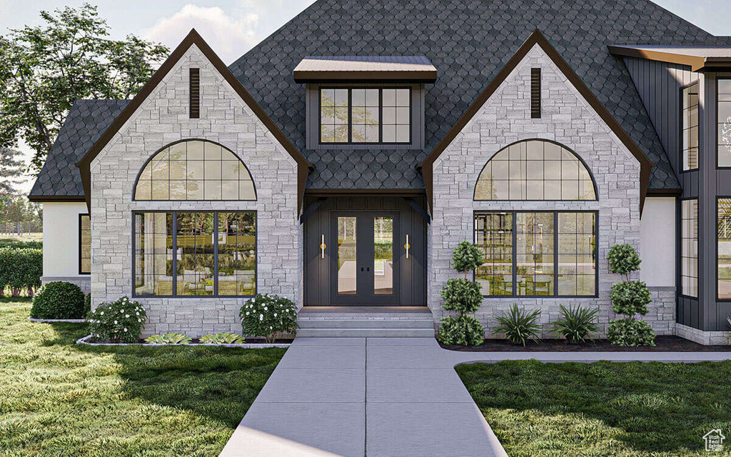 View of exterior entry featuring a lawn, board and batten siding, french doors, and stone siding