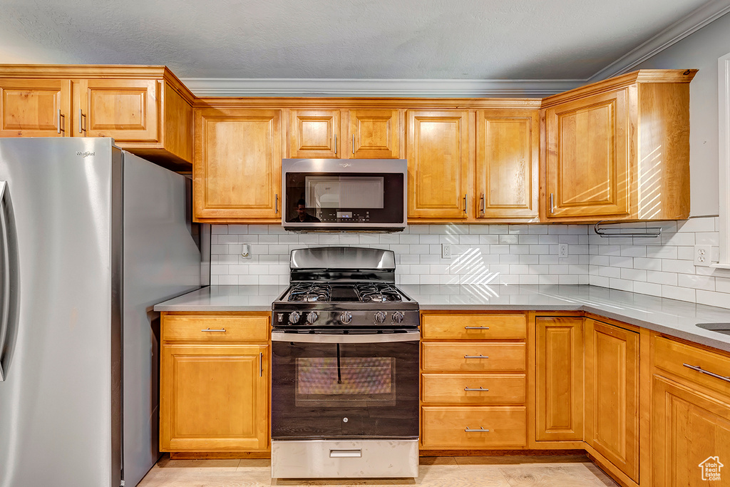 Kitchen with stainless steel appliances, ornamental molding, light countertops, decorative backsplash, and brown cabinetry