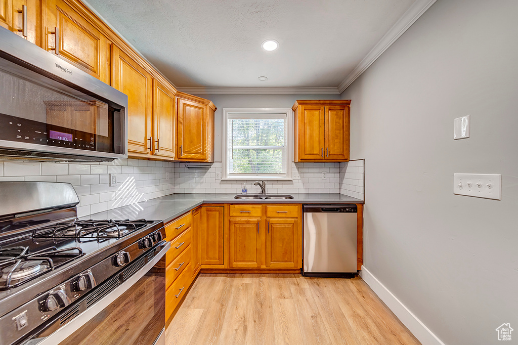 Kitchen featuring stainless steel appliances, a sink, light wood-style flooring, crown molding, and brown cabinets