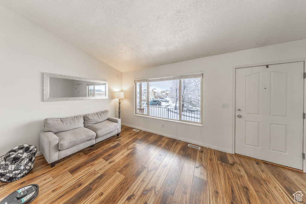 Living room featuring vaulted ceiling, a textured ceiling, hardwood / wood-style floors, plenty of natural light, and baseboards