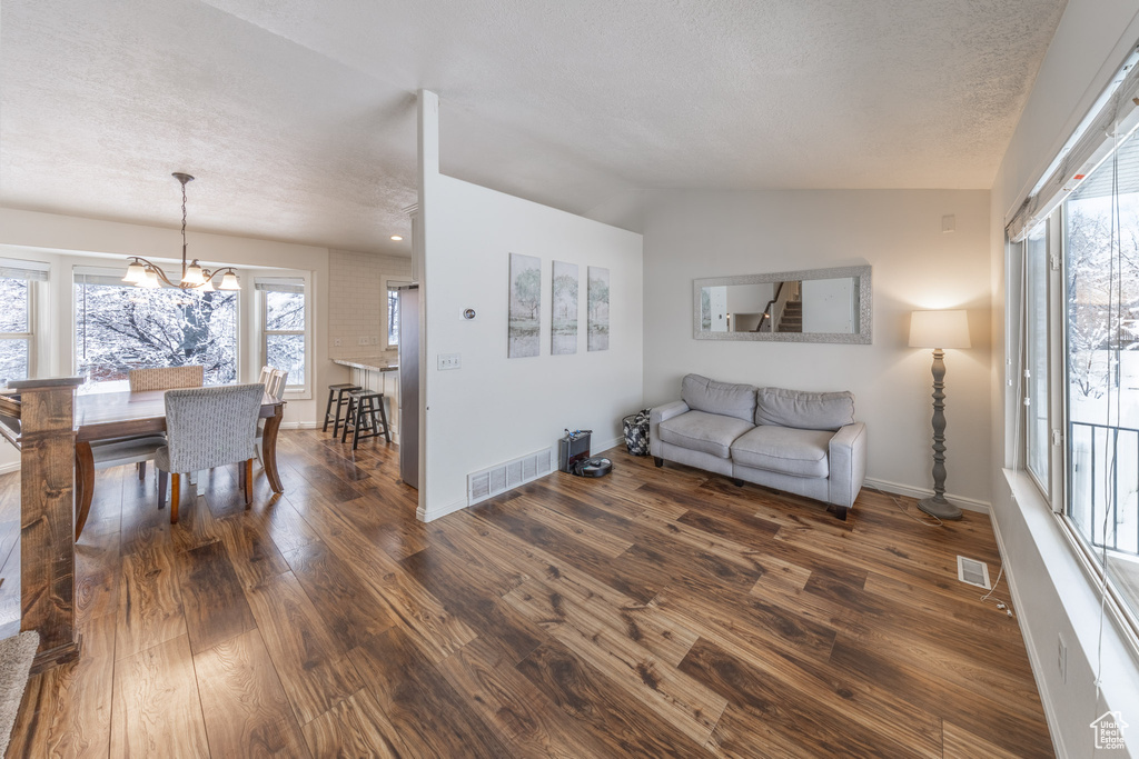 Living room featuring dark wood-style flooring, a chandelier, a textured ceiling, plenty of natural light, and baseboards