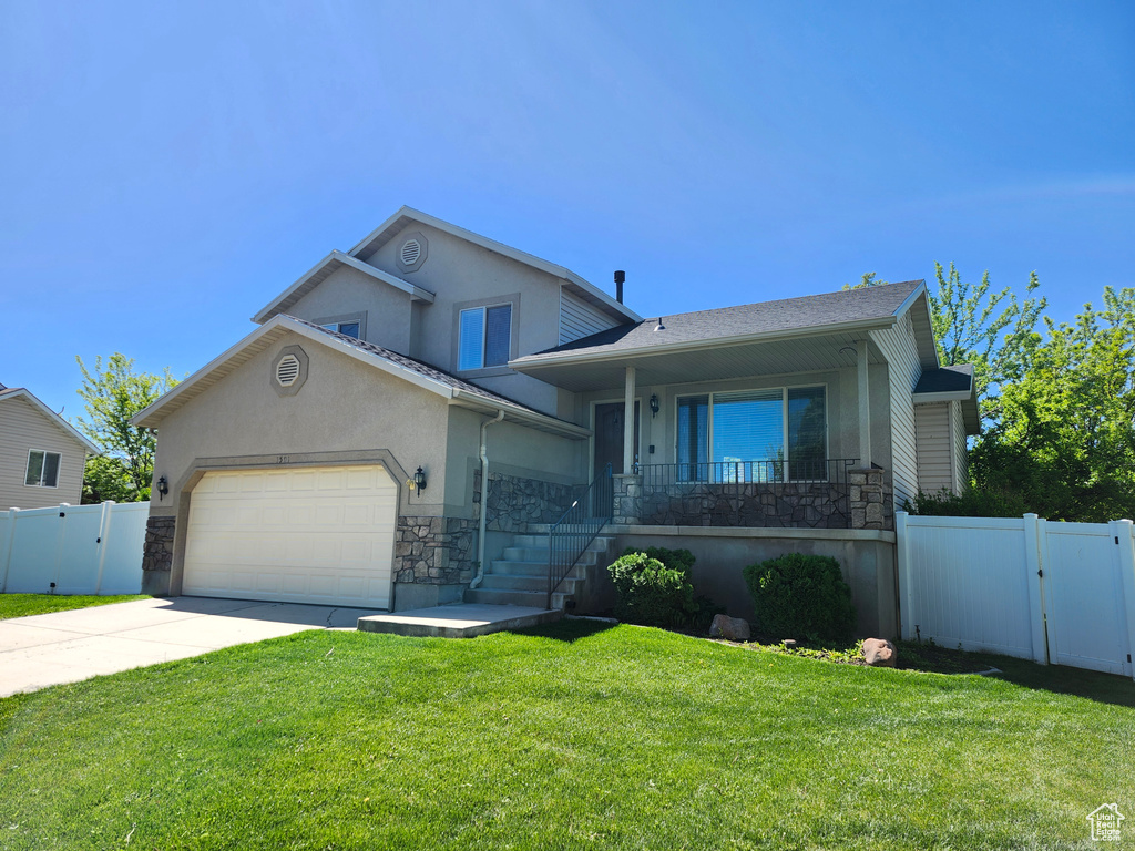 Split level home featuring a gate, stone siding, stucco siding, driveway, and an attached garage