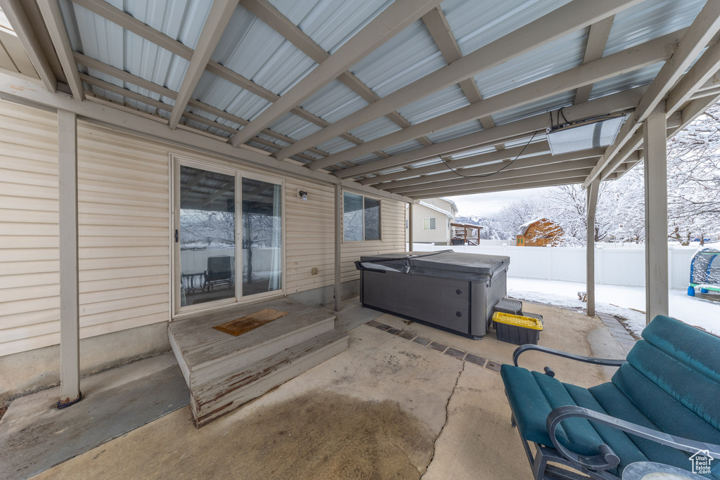 Snow covered patio with a hot tub and fence