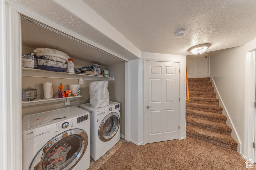 Clothes washing area featuring light colored carpet, washing machine and dryer, a textured ceiling, and baseboards