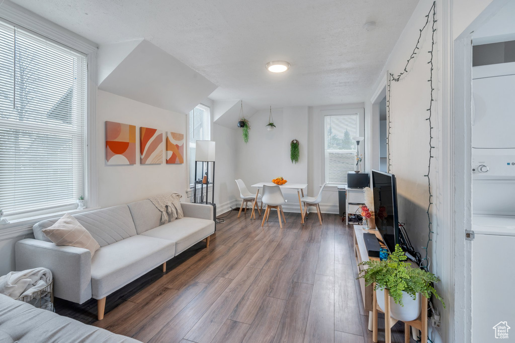 Living area with stacked washing machine and dryer, wood finished floors, and baseboards