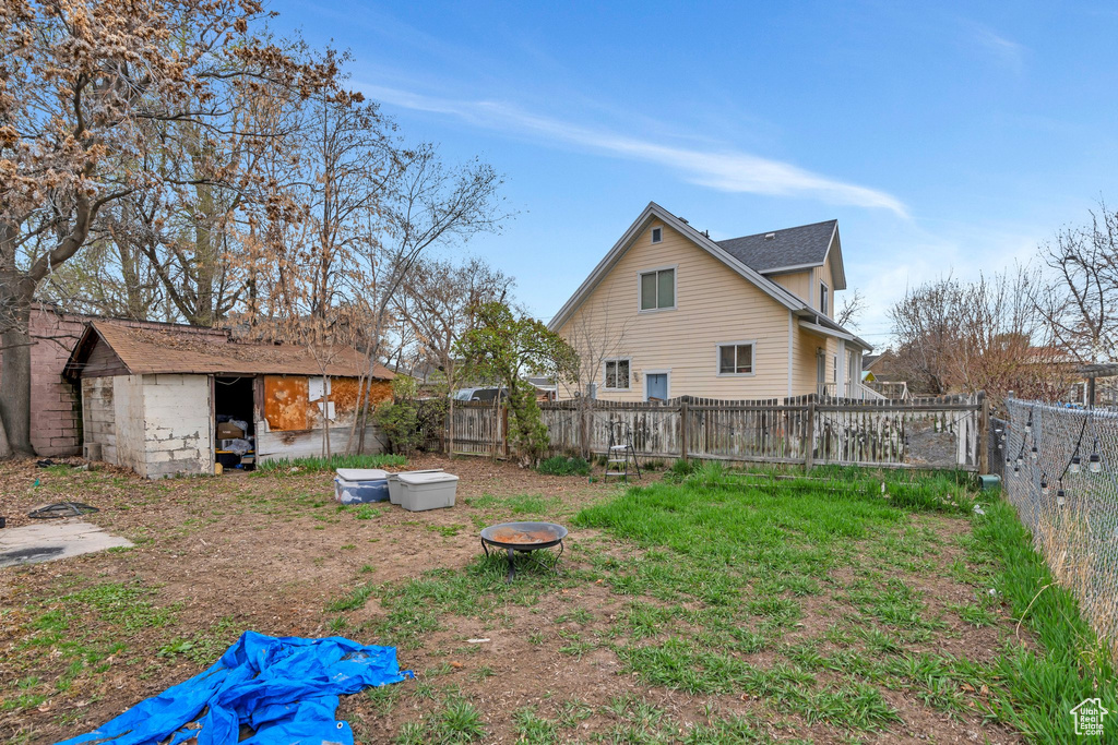 Fenced backyard with a fire pit, a storage shed, and an outbuilding