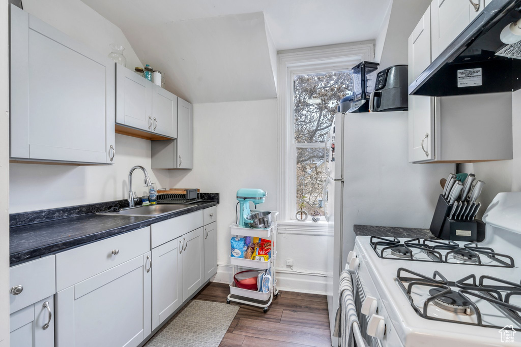 Kitchen with white gas range oven, a sink, dark countertops, under cabinet range hood, and dark wood-type flooring