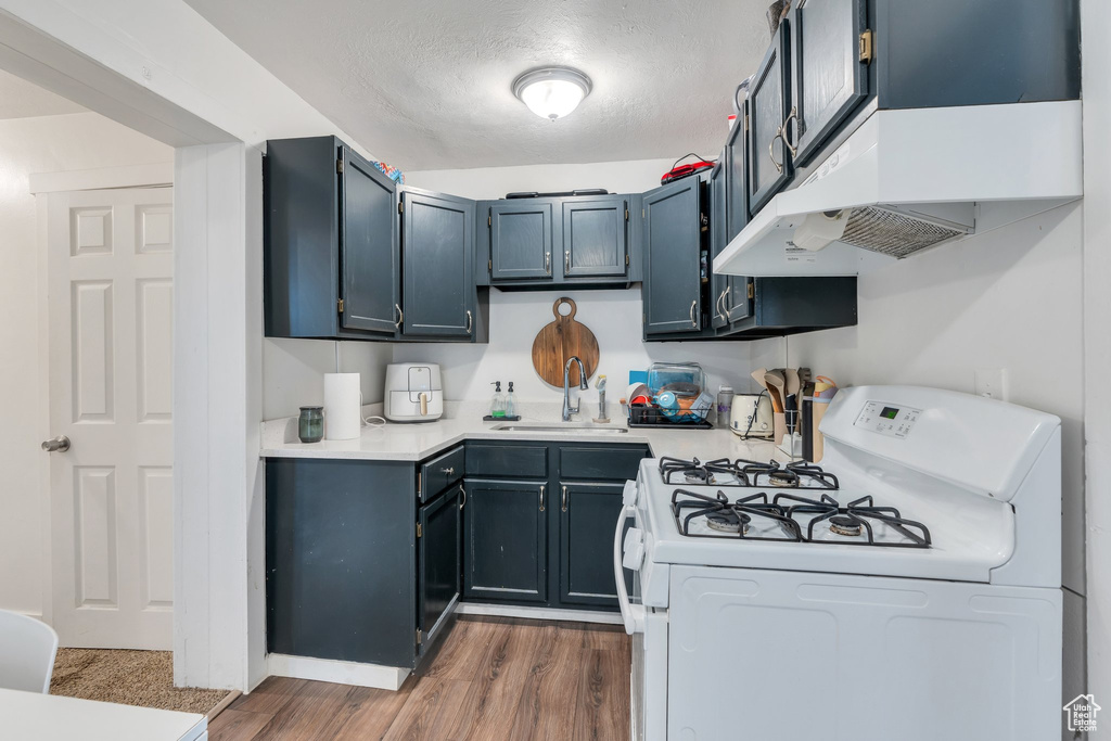 Kitchen featuring white gas range oven, a sink, light countertops, dark wood-type flooring, and a textured ceiling