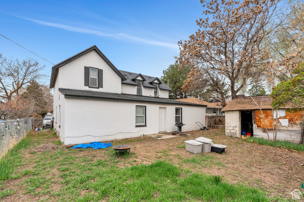 Back of house with stucco siding, a fenced backyard, a storage unit, and an outbuilding