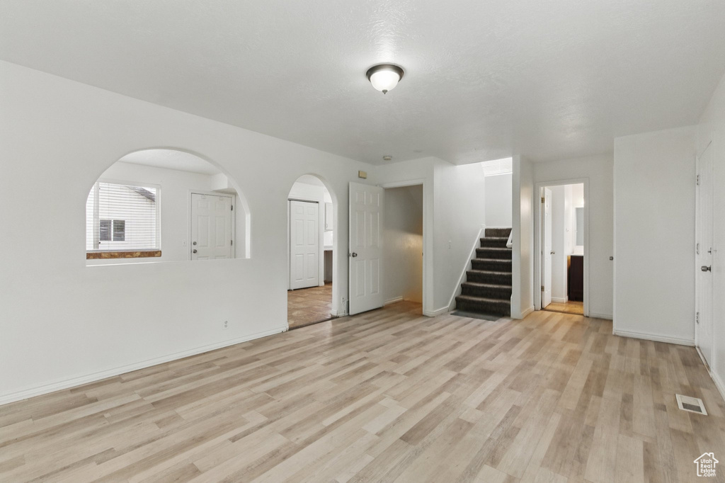Unfurnished living room featuring stairway, light wood-style flooring, baseboards, and arched walkways